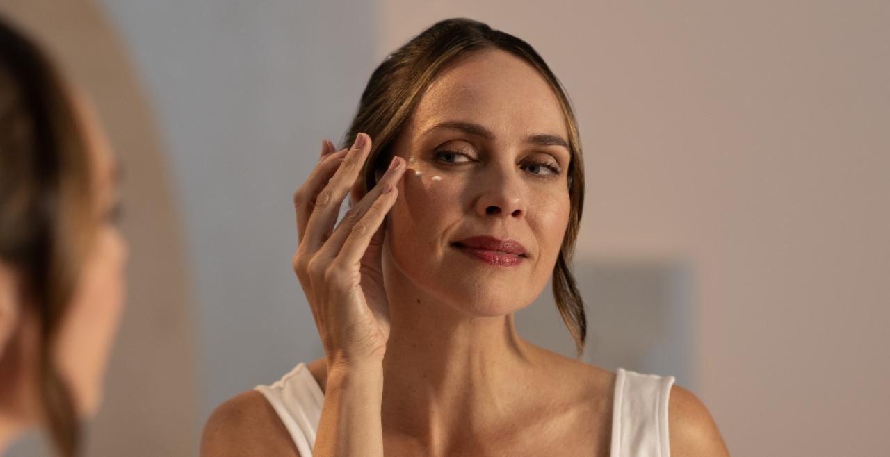 lady looking in a mirrior and applying eye cream to her under eyes